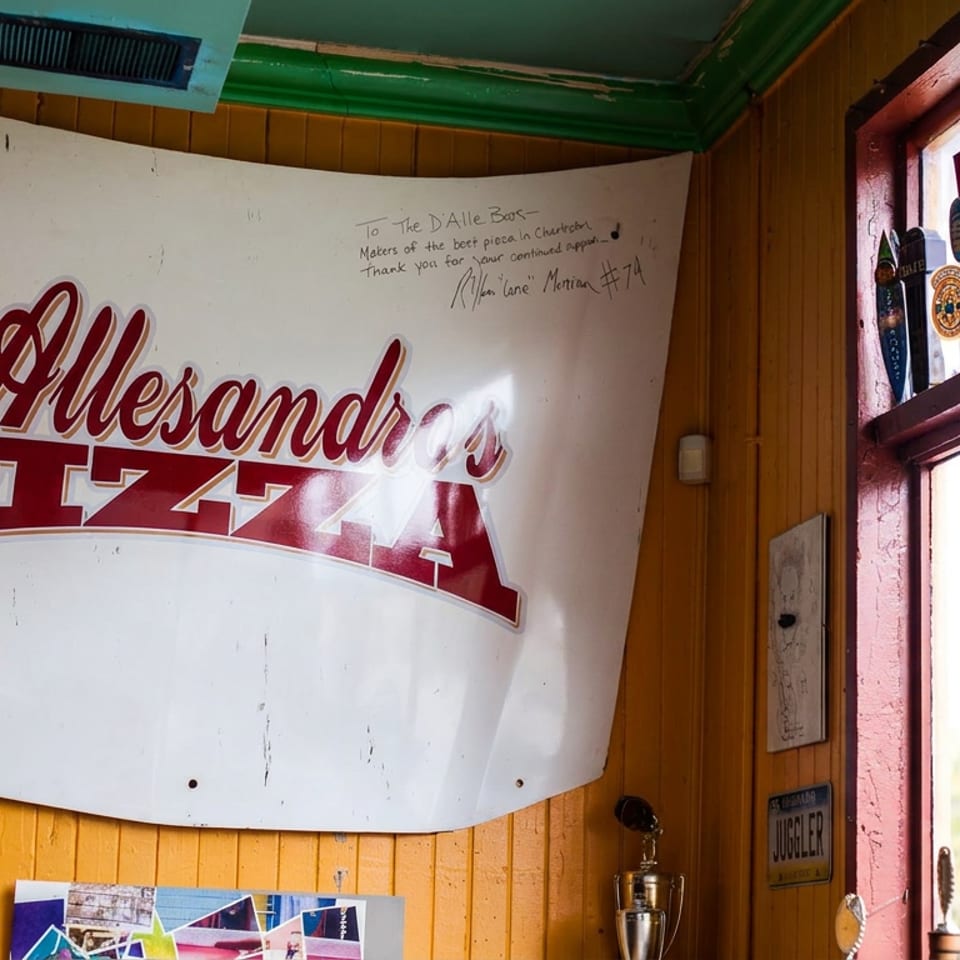 Vintage D'Alessandro's Pizza sign displayed on a wood-paneled wall beside a sunny window with beer taps.