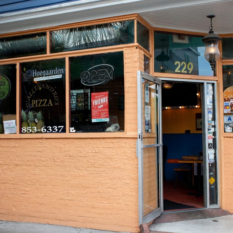 Exterior of a blue-and-orange pizzeria with open glass door, palm trees, visible pizza signage, and address 229.