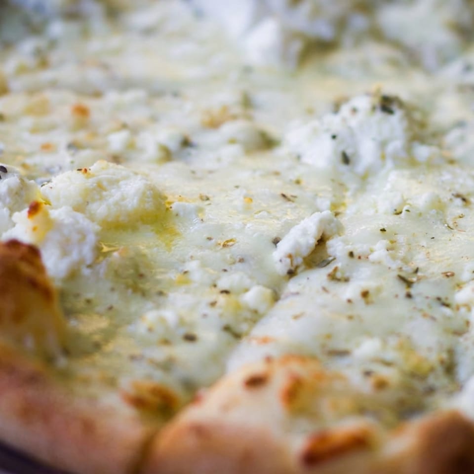 Close-up of a golden-baked pizza topped with melted white cheese, herbs, and browned crust.