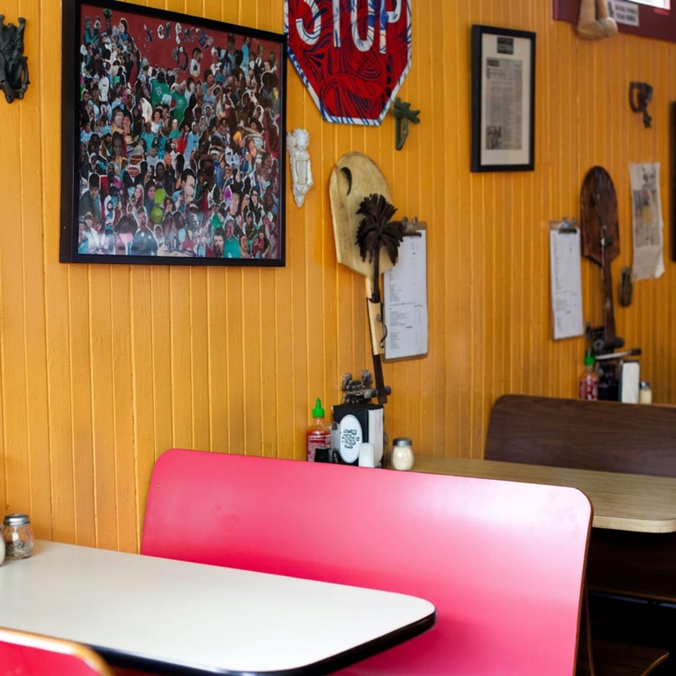 Retro diner interior with orange wood-paneled walls, red booths, dark wooden tables, vintage artwork, and decorative wall displays.