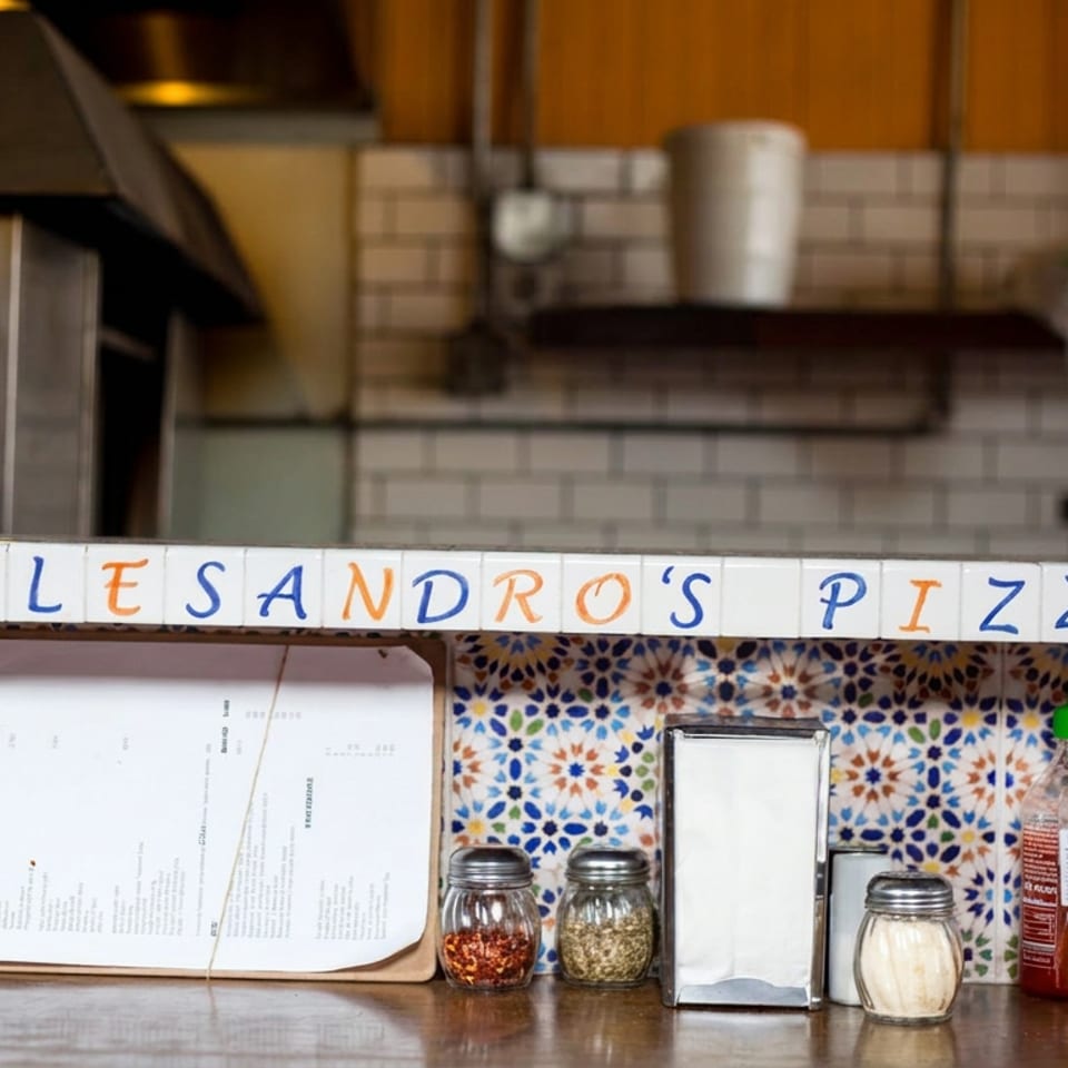 D’Alessandro’s Pizza counter with patterned tile backsplash, menus, napkin holder, spices, and hot sauce.